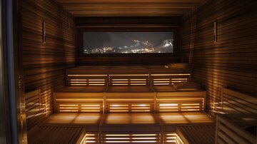 A cozy sauna with wooden shelves and soft lighting. Through the window, there is a beautiful view of the mountains.