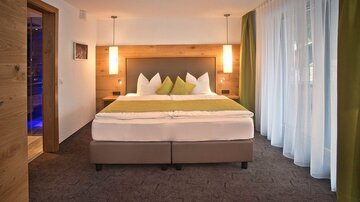 A modern bedroom with a large double bed and green accents.  
Large windows provide plenty of light and a welcoming atmosphere.