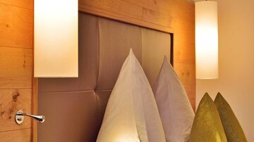 A modern bedroom with a cozy bed setup. The subtle lamps and wooden walls create a warm atmosphere.