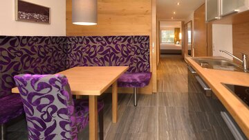 A modern kitchen with a dining area in shades of purple. The space is bright and inviting, with wooden details and cozy seating.