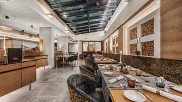 Ein modernes Restaurant mit eleganten Tischen und Stühlen. Große Fenster sorgen für viel Tageslicht und eine einladende Atmosphäre.