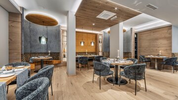 Ein modernes Restaurant mit stilvollen runden Tischen und bequemen Stühlen. Die Wände sind in neutralen Tönen gehalten, ergänzt durch ansprechende Beleuchtungselemente.