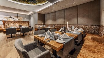 Ein elegantes Restaurant mit modernen Tischen und Stühlen. Die gedeckten Tische sind geschmackvoll dekoriert und schaffen eine einladende Atmosphäre.