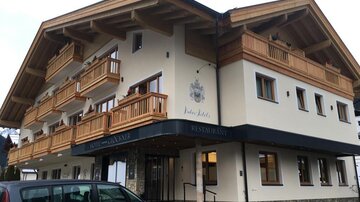 Ein modernes Gebäude im alpinen Stil mit Holzbalkonen. Darunter befindet sich ein Restaurant und ein Parkplatz.