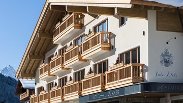 Ein charmantes Hotel mit Holzbalconen und einem modernen alpinen Design. Die Umgebung zeigt schneebedeckte Berge im Hintergrund.