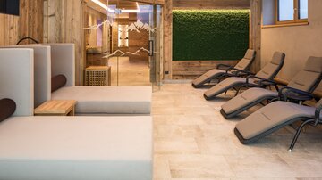 Ein moderner Wellnessbereich mit bequemen Liegen und einer gemütlichen Atmosphäre. Die Wände sind aus Holz und es gibt eine grüne Pflanzenwand.