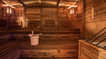 Eine Sauna mit Holzwänden und Sitzbänken. In der Mitte steht ein Holz-Eimer.