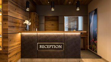 Eine moderne Hotelrezeption mit Holzverkleidung und eleganten Lampen. Der Empfangstresen ist gut beleuchtet und ansprechend gestaltet.