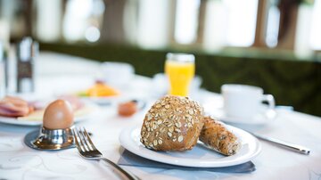 Ein delikates Frühstück mit einem Brötchen, einem Ei und frischem Obst. Dazu gibt es ein Glas Orangensaft.
