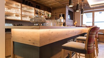 Eine stilvolle Bar mit Holzdetails und eleganten Stühlen. Im Hintergrund sind Flaschen und Gläser gut sichtbar.