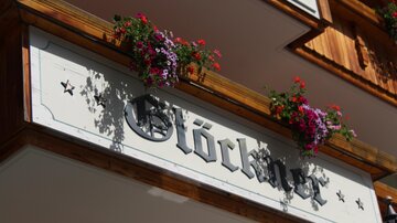 Ein Holzschild mit der Aufschrift „Glöckner“ und bunten Blumen. Die Dekoration verleiht dem Ort eine einladende Atmosphäre.