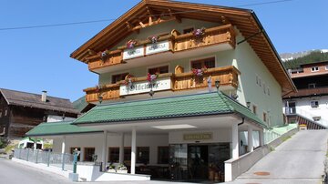 Ein gemütliches Haus mit einem traditionellen alpenländischen Stil. Die Fassade ist mit blühenden Blumen und Holzelementen geschmückt.
