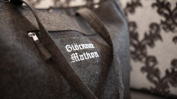 Eine elegante schwarze Tasche aus Filz mit dem Schriftzug „Glöckner Marthon“. Der Hintergrund zeigt ein gemustertes Kissen.