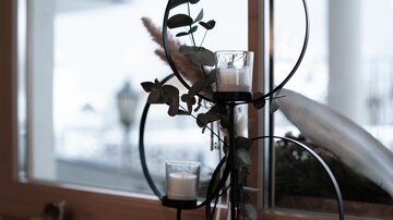 Eine stilvolle Dekoration mit Kerzen und Pflanzen in einem modernen Halter. Die Komposition steht auf einer Fensterbank und bietet einen eleganten Look.