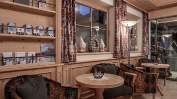 Eine gemütliche Sitzecke mit zwei Stühlen und einem Tisch aus Holz. Die Wände sind aus Holz mit dekorativen Vorhängen und Fenstern, die viel Licht hereinlassen.