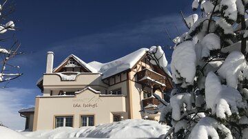 A house in winter, surrounded by deep snow. The sky is clear and blue, while the blanket of snow covers the landscape.