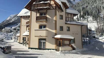 A snow-covered building in a winter landscape. The mountains in the background are clear and the sun is shining.