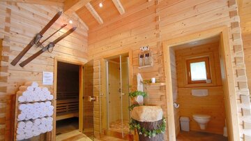 A wooden interior with a sauna and a shower area. Towels are neatly stacked and skis are hung on the wall.