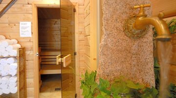 A relaxing wellness area with a sauna and a brass faucet. Towels are neatly stacked beside the sauna.