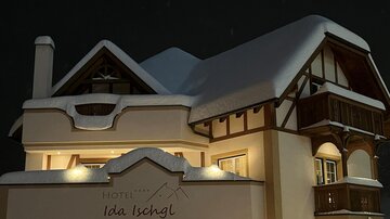 A beautifully lit hotel building in winter with a thick layer of snow on the roof. The architecture is traditional and inviting.