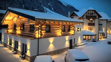 A cozy wooden house in the snow, warmly lit. The surroundings are wintry with a tranquil atmosphere.