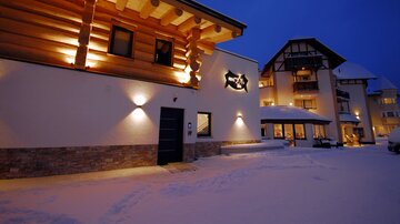 A cozy building in the snow, illuminated by warm lights. The sky is dark blue and there is fresh snow on the ground.