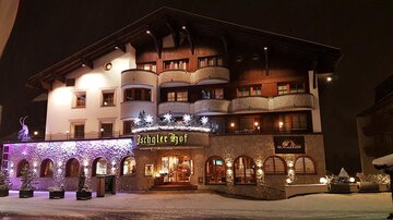 Ein gemütliches Hotelgebäude im Winter, beleuchtet von farbigen Lichtern. Schnee bedeckt den Boden und verleiht der Szene eine festliche Atmosphäre.