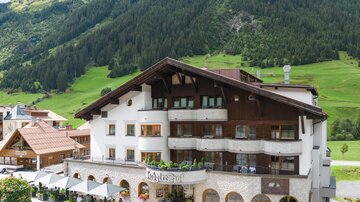 Ein charmantes Hotel in den Bergen mit traditionellen Holzelementen. Umgeben von einer malerischen Landschaft und grünen Wiesen.