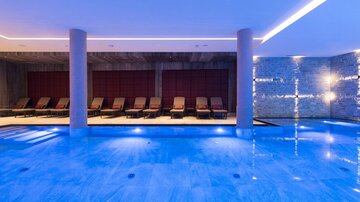 Ein moderner Wellnessbereich mit einem klaren blauen Pool und eleganten Liegen. Sanfte Beleuchtung schafft eine entspannende Atmosphäre.