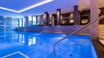 Ein luxuriöser Innenpool mit klarem, blauem Wasser. Die Umgebung ist modern und elegant mit entspannenden Liegestühlen.
