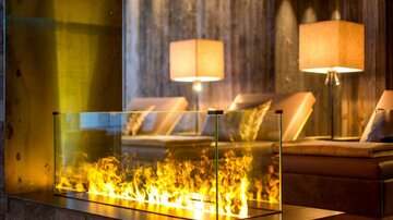 Ein modernes Wohnzimmer mit einer Glasfeuerstelle und warmem Licht. Angenehme Atmosphäre mit eleganten Möbeln und sanfter Beleuchtung.