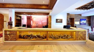 Eine moderne Hotelrezeption mit einem kunstvoll gestalteten Holzempfangstresen. Im Hintergrund sind gemütliche Sitzgelegenheiten und Dekorationen sichtbar.