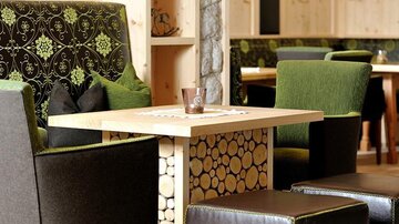 Ein gemütlicher Sitzbereich mit stilvollen Stühlen und einem Holztisch. Die modernen Möbel sind in Grün- und Brauntönen gehalten und schaffen eine einladende Atmosphäre.