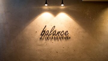 Ein minimalistisches Wanddesign mit der Aufschrift "balance" in eleganter Schrift. Zwei Deckenleuchten beleuchten den Schriftzug.