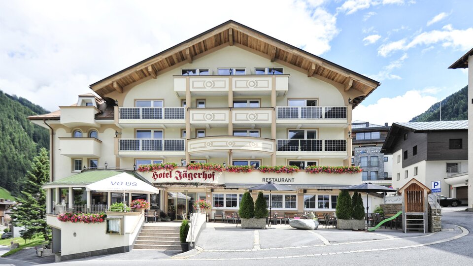 A cozy hotel with an inviting entrance. The facade is bright and designed in typical alpine style, surrounded by mountains.