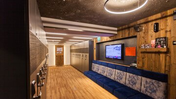 A modern changing room with wooden and fabric elements. Lockers are hanging on the wall, and a television is visible.