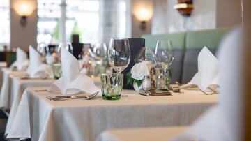 An elegantly set table in a restaurant with white tablecloths, crystal glasses, and decorative elements. The atmosphere is inviting and tasteful.