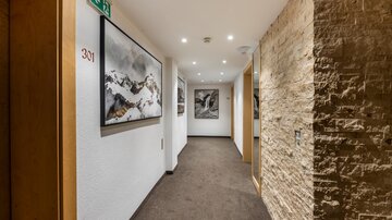 A bright hallway with soft lighting and a combination of smooth and textured walls. Pictures of mountain landscapes hang on the walls.