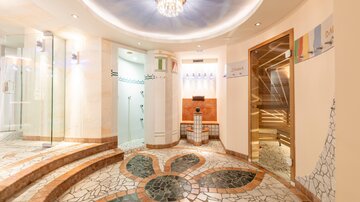 An elegant spa area with a stylish floor pattern and soft, relaxing colors. The walls are equipped with glass showers and wooden paneling.