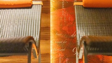 Two stylish loungers stand before a warm, orange wall with flowing script. The floor is made of light tiles with a green border.