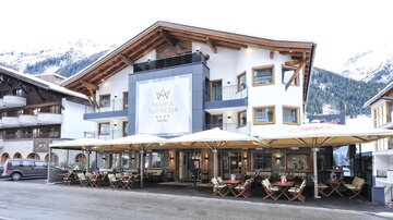 A modern hotel with an inviting terrace and mountain views. The architecture is traditionally and elegantly designed.