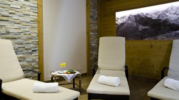 A peaceful wellness area with lounge chairs and a beautiful view of the mountains. A small table with two drinks and fresh fruit creates a relaxed atmosphere.