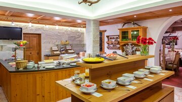 A cozy dining room with a buffet decorated with fresh fruits and dishes. Wooden furniture and blooming plants create an inviting atmosphere.