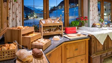 A cozy breakfast buffet with fresh rolls and pastries. In the background, snow-capped mountains and an inviting view can be seen.