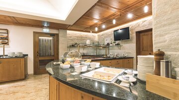 A modern kitchen with wooden shelves and a large countertop. Various dishes are arranged in bowls on the buffet.