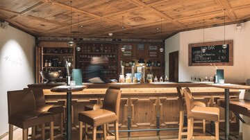 A cozy bar with wooden paneling and wooden furniture. The bar counter is well-stocked with drinks and has an inviting atmosphere.
