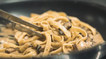 A dish with freshly made fettuccine in a creamy sauce. The pasta is garnished with mushrooms and served with tongs.