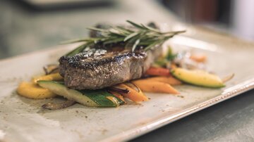A juicy piece of meat on a plate, surrounded by colorful vegetables. Fresh herbs add extra flavor to the dish.