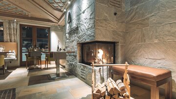 A cozy interior with an open fireplace and modern stone wall. The warm colors and stylish furnishings create an inviting atmosphere.