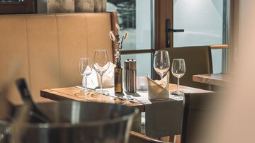 An elegantly set table in a restaurant, surrounded by stylish chairs. Several glasses and a bottle are placed on the table.